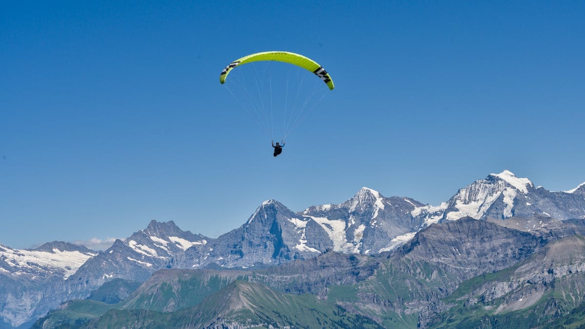 Paraglider soaring over the stunning Swiss Alps on a clear summer day.